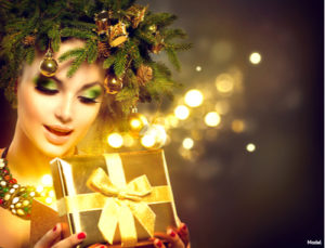 Woman wearing a wreath of pine tree branches and ornaments opens a gift