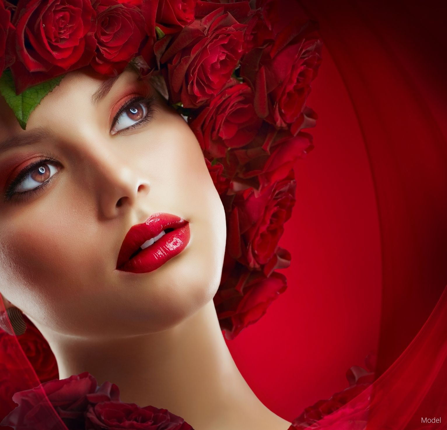 Woman in red lipstick and red eye makeup with a wreath of red roses on her head in front of a red background