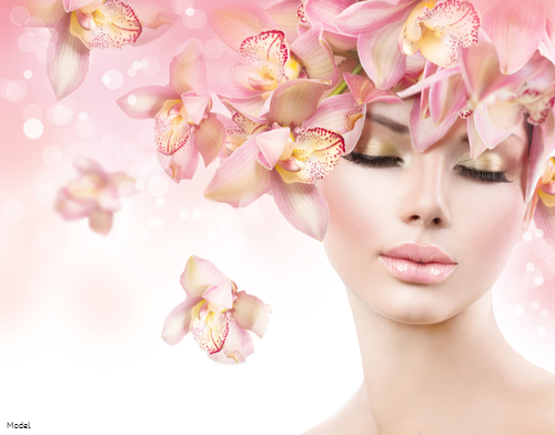 Relaxed woman with glowing skin surrounded by pink orchids