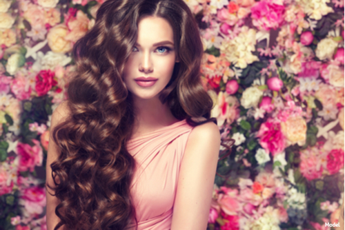 Stunning woman with long brown hair in front of a background of pink and white flowers