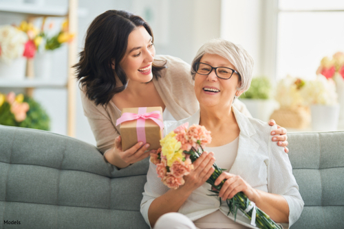 Adult daughter surprising her older mother with gifts and flowers