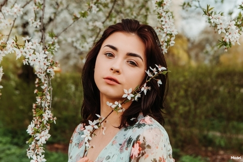 Young woman outdoors standing among trees blooming small white flowers