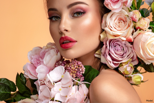 Woman wearing red lipstick and pink eye makeup surrounded by pink and white flowers