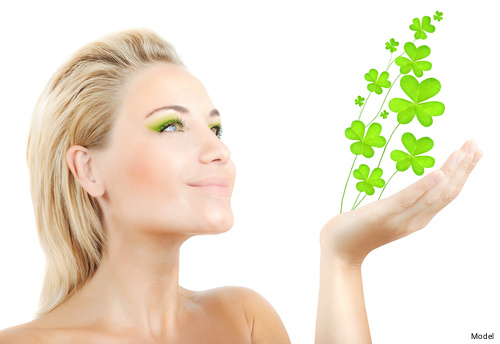 Woman with blonde hair wearing green eyeshadow with four leaf clovers sprouting from her hand